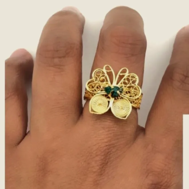 Anillo de mariposa de filigrana dorada con dos esmeraldas en bruto, puesto en la mano.