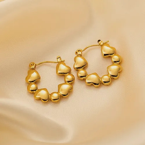 Aretes de aro dorado formados por corazones macizos encadenados, sobre seda color crema.