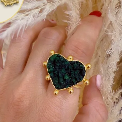Anillo con esmeralda en bruto en forma de corazón sujeta por garras doradas, puesto en la mano.