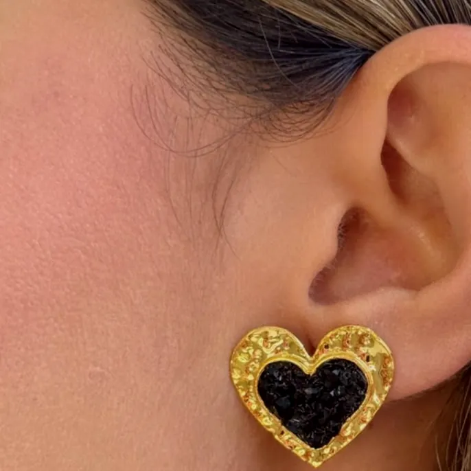 Arete de corazón en piedra negra con marco dorado, puesto en la oreja.