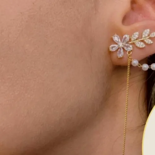 Ear cuff de hojas de circonita unido por cadena de perlas a un pendiente largo, puesto en la oreja.