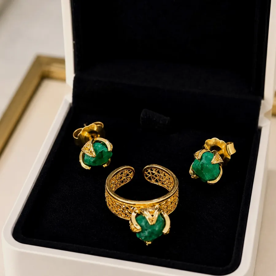 Ring and earrings with raw emerald set in gold tone, inside a black case.