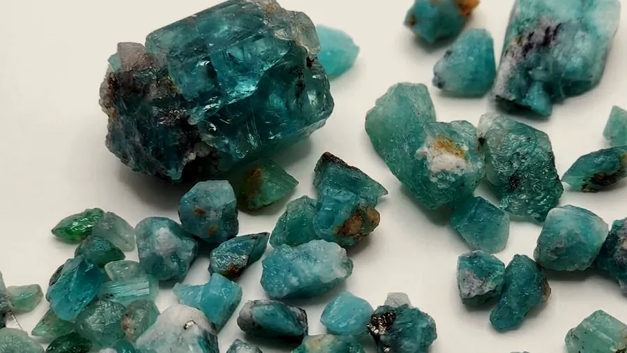 Raw emeralds of various sizes on a light background.