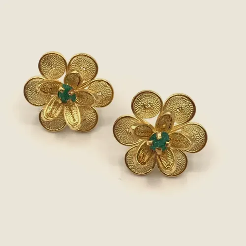 Aretes de filigrana dorada en forma de flor de cinco pétalos con una esmeralda en bruto en el centro.