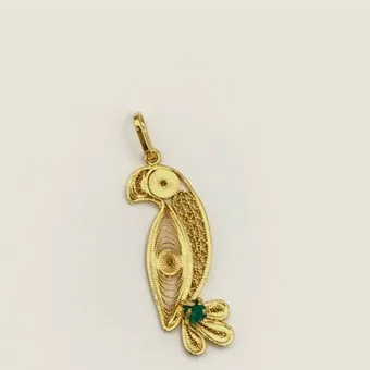 Gold-tone filigree pendant shaped as a macaw, the body filled with spirals and a raw emerald in the tail.