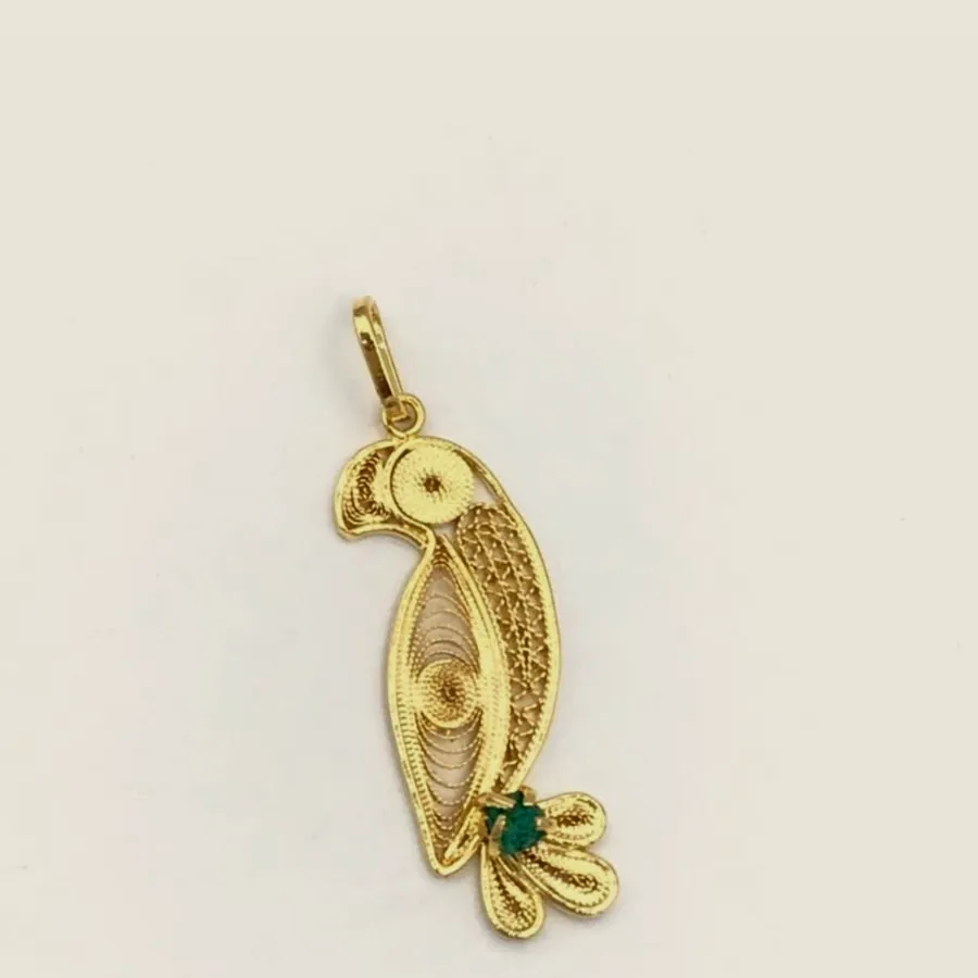 Gold-tone filigree pendant shaped as a macaw, the body filled with spirals and a raw emerald in the tail.