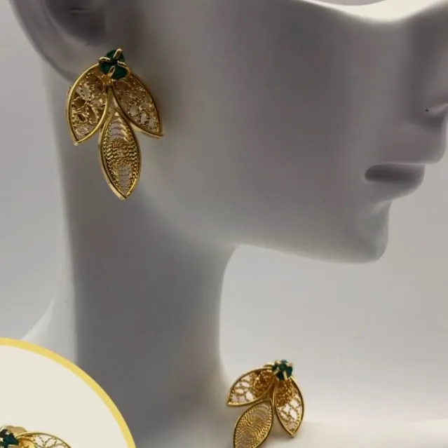 Aretes de filigrana dorada en forma de hoja sobre un busto blanco.