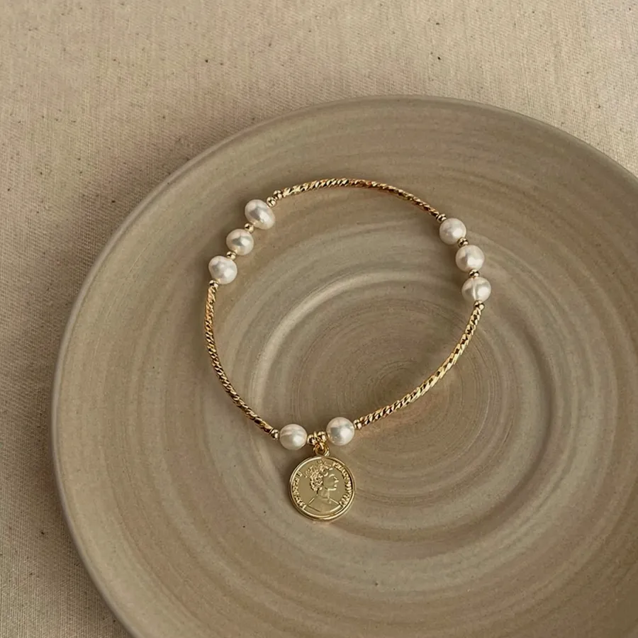 Bracelet of gold-tone beads and pearls with an engraved medallion hanging.