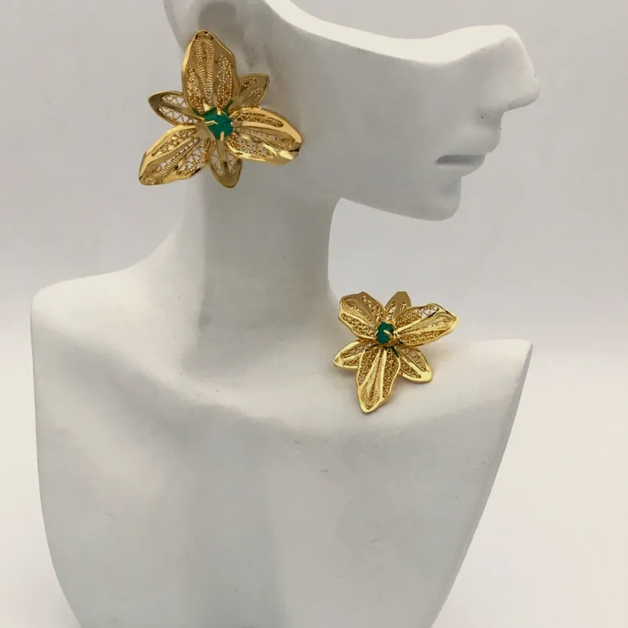 Gold-tone five-petal flower earrings with a raw emerald, on a white bust.