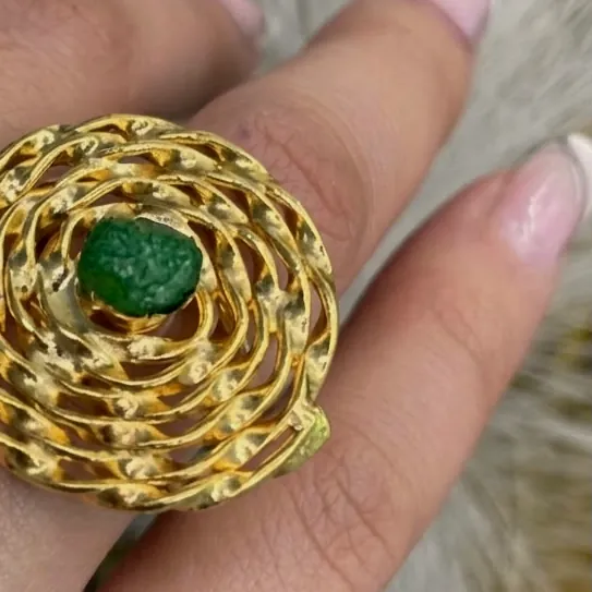 Anillo de espiral dorada con esmeralda en bruto en el centro, puesto en la mano.