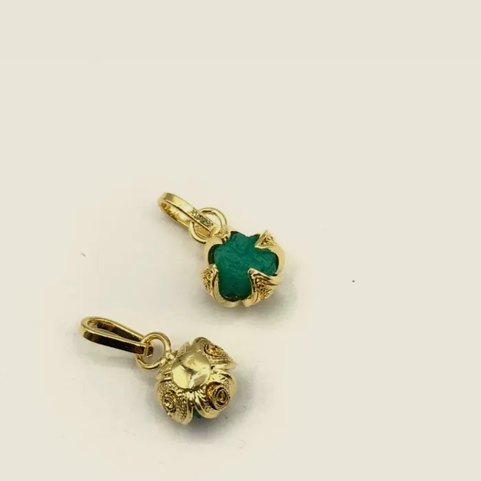 Dos dijes de trébol, uno con esmeralda en bruto verde y otro dorado liso.