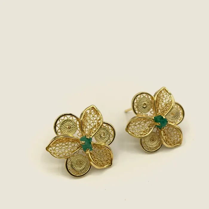 Aretes de filigrana dorada de cuatro pétalos con esmeralda en bruto en el centro.
