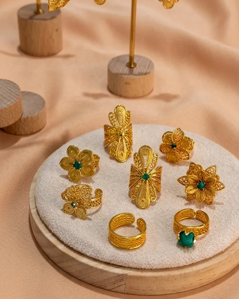 Anillos y aretes de filigrana dorada con piedras verdes sobre tela color durazno.