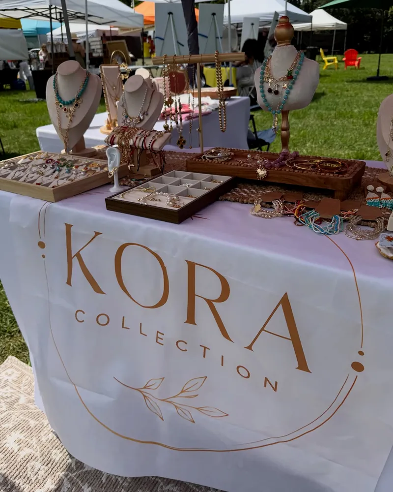 Mesa de KORA en el mercado al aire libre, con bustos y expositores de joyería.