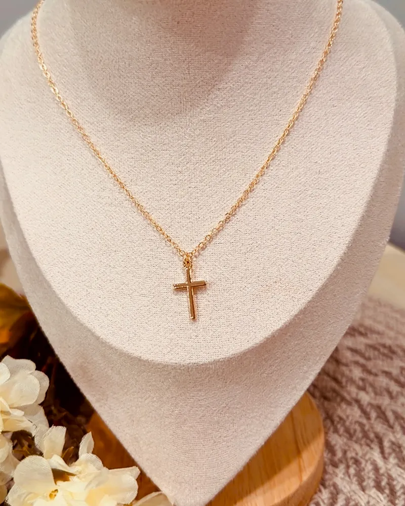 Collar dorado con dije de cruz sobre un busto de terciopelo crema.