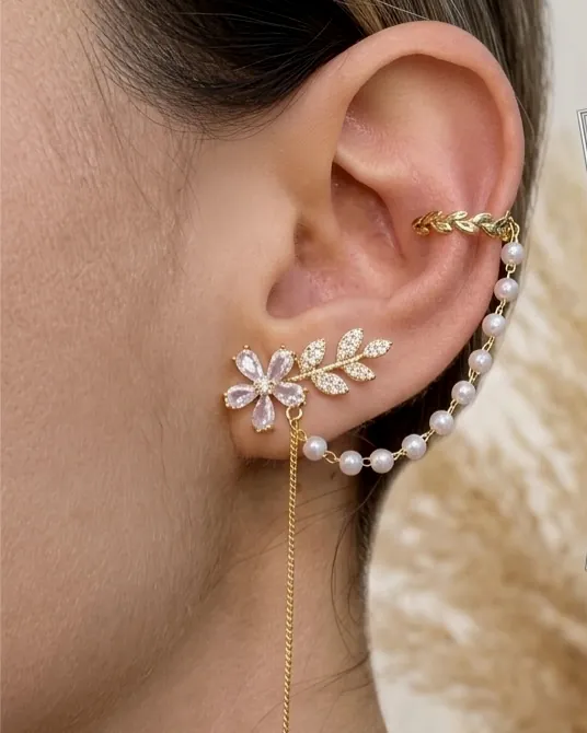 Aretes de flor, arracada de perlas y ear cuff puestos en la oreja.