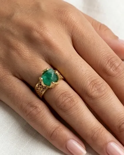 Anillo de filigrana dorada con piedra verde puesto en la mano.