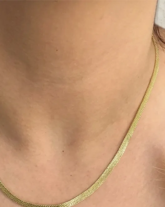 Cadena tejida dorada puesta al cuello.